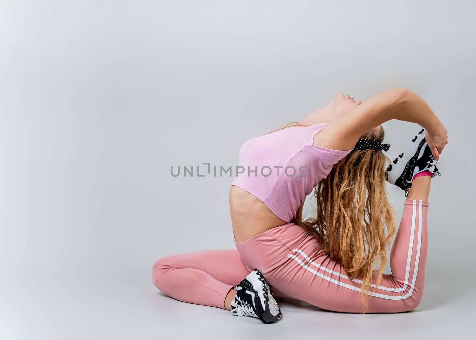 Fitness, sport, training and lifestyle concept. Athletic acrobat woman wearing pink sportswear doing yoga in the studio isolated on gray background