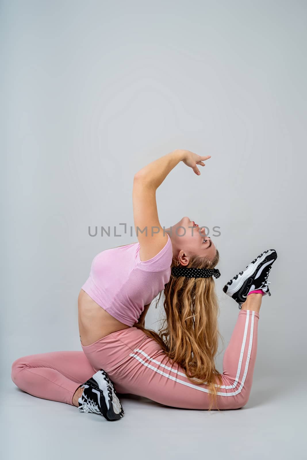 Fitness, sport, training and lifestyle concept. Acrobat woman wearing pink sportswear working out in the studio isolated on gray background with copy space