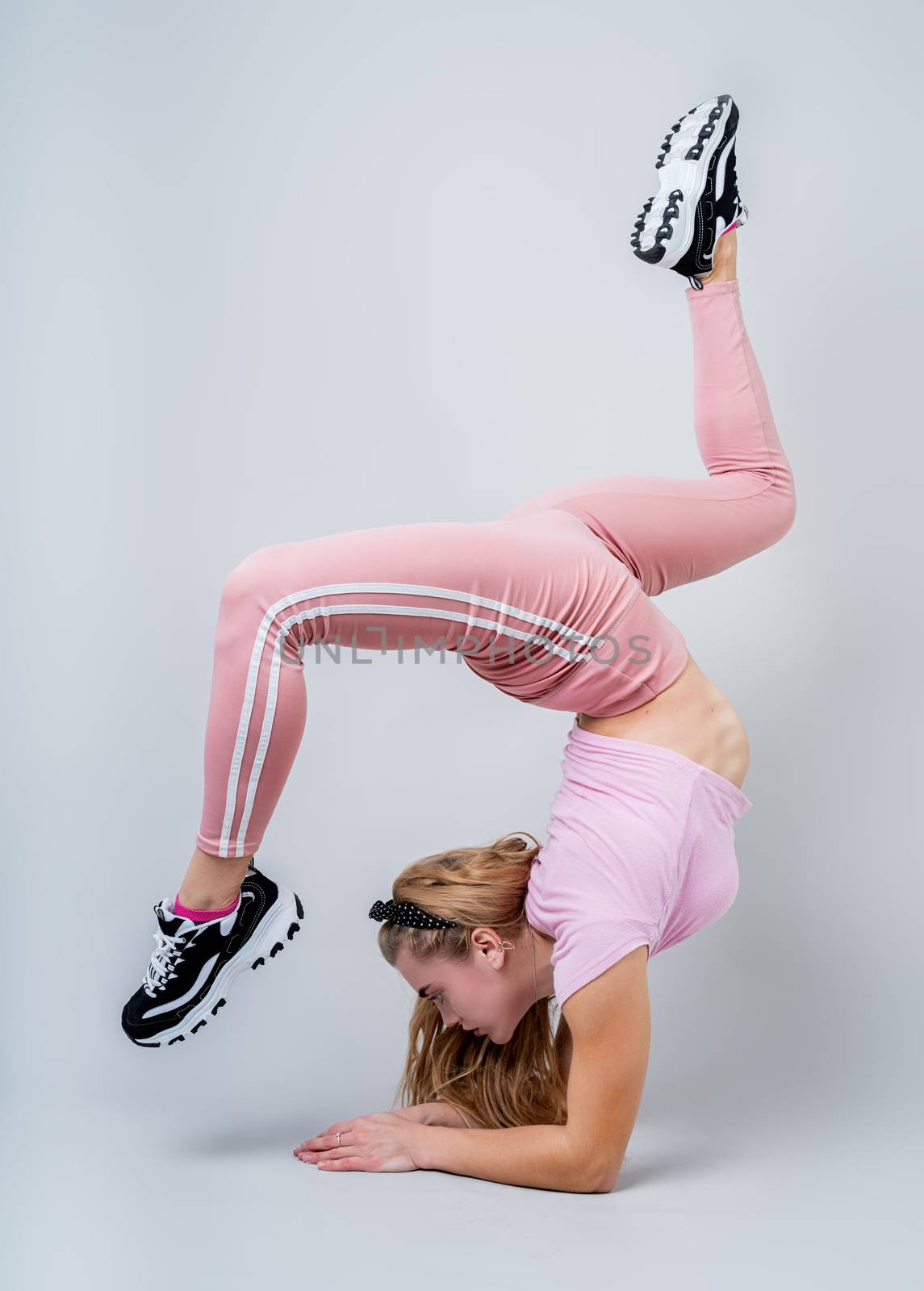Fitness, sport, training and lifestyle concept. Acrobat woman wearing pink sportswear working out in the studio isolated on gray background with copy space