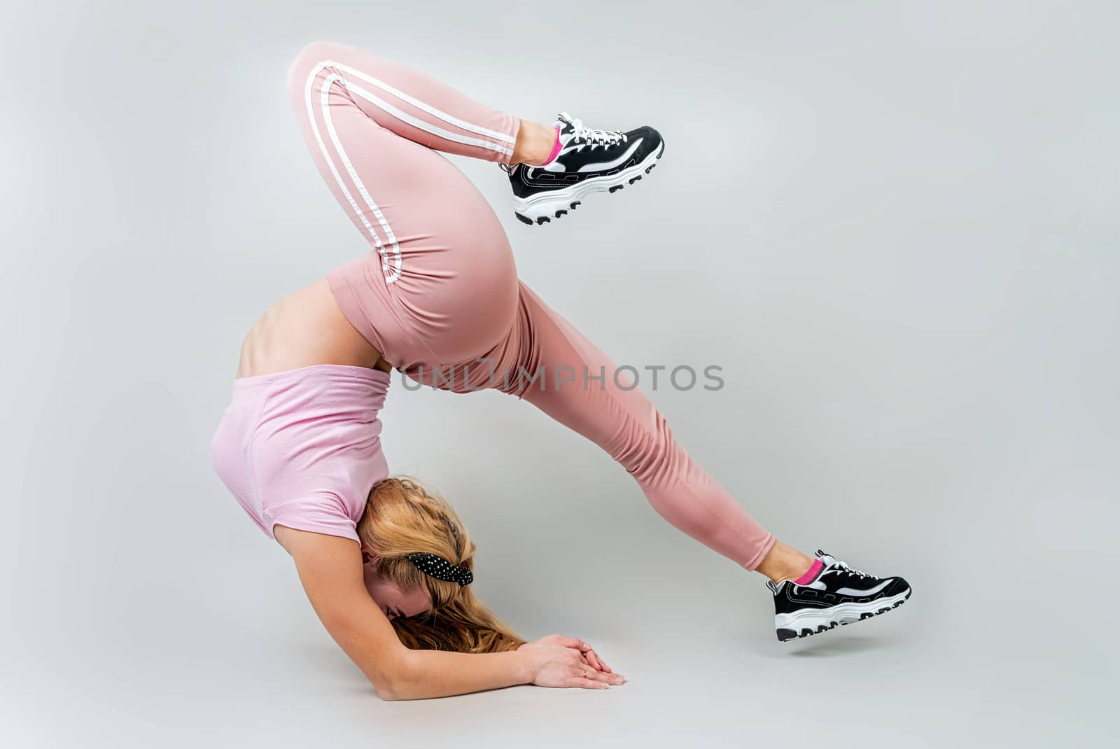 Acrobat woman wearing pink sportswear working out in the studio isolated on gray background by Desperada
