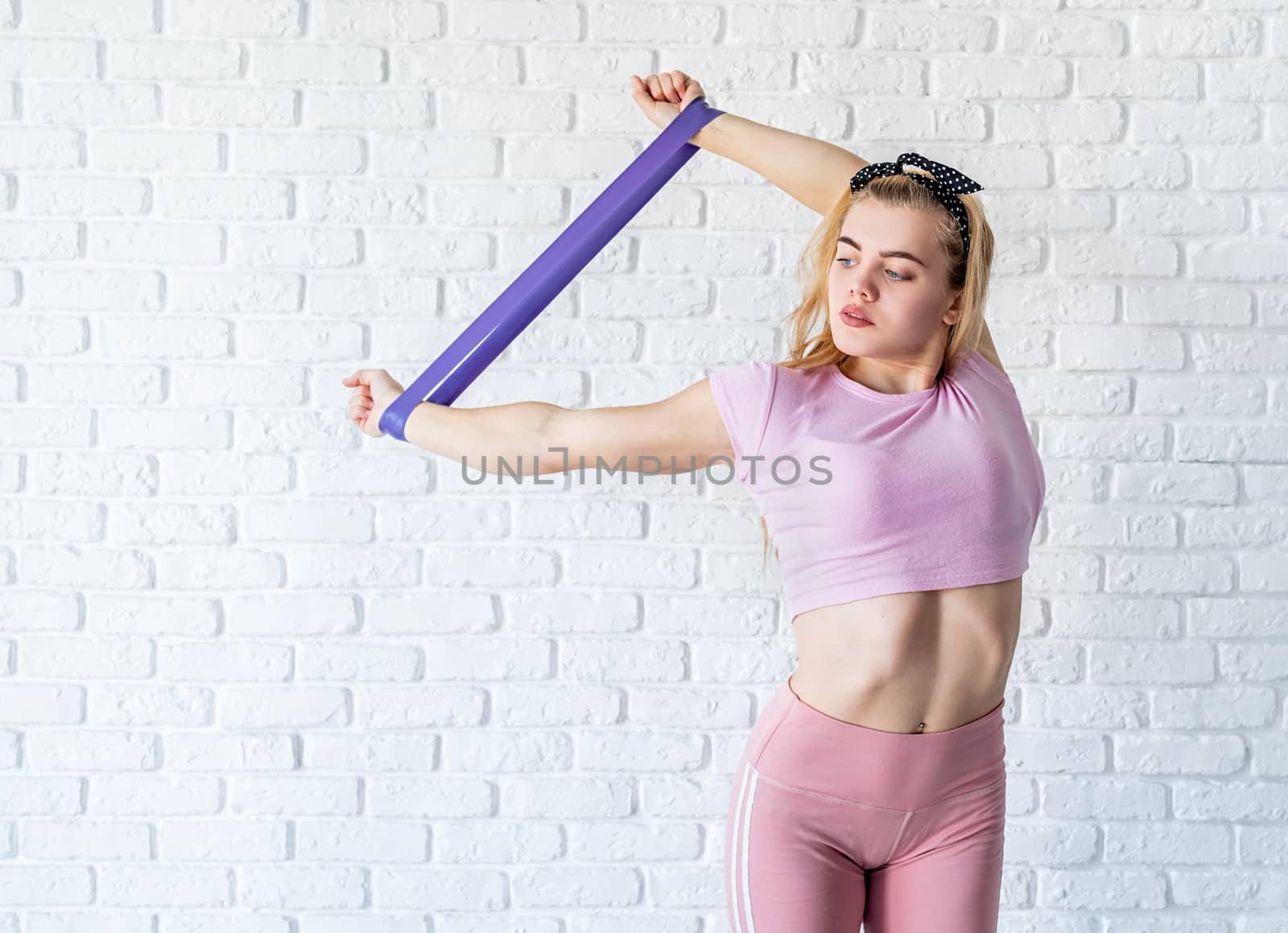 Fitness, sport, training and lifestyle concept. Staying home. Athletic woman doing exercises using a resistance band at home at white brick wall background with copy space