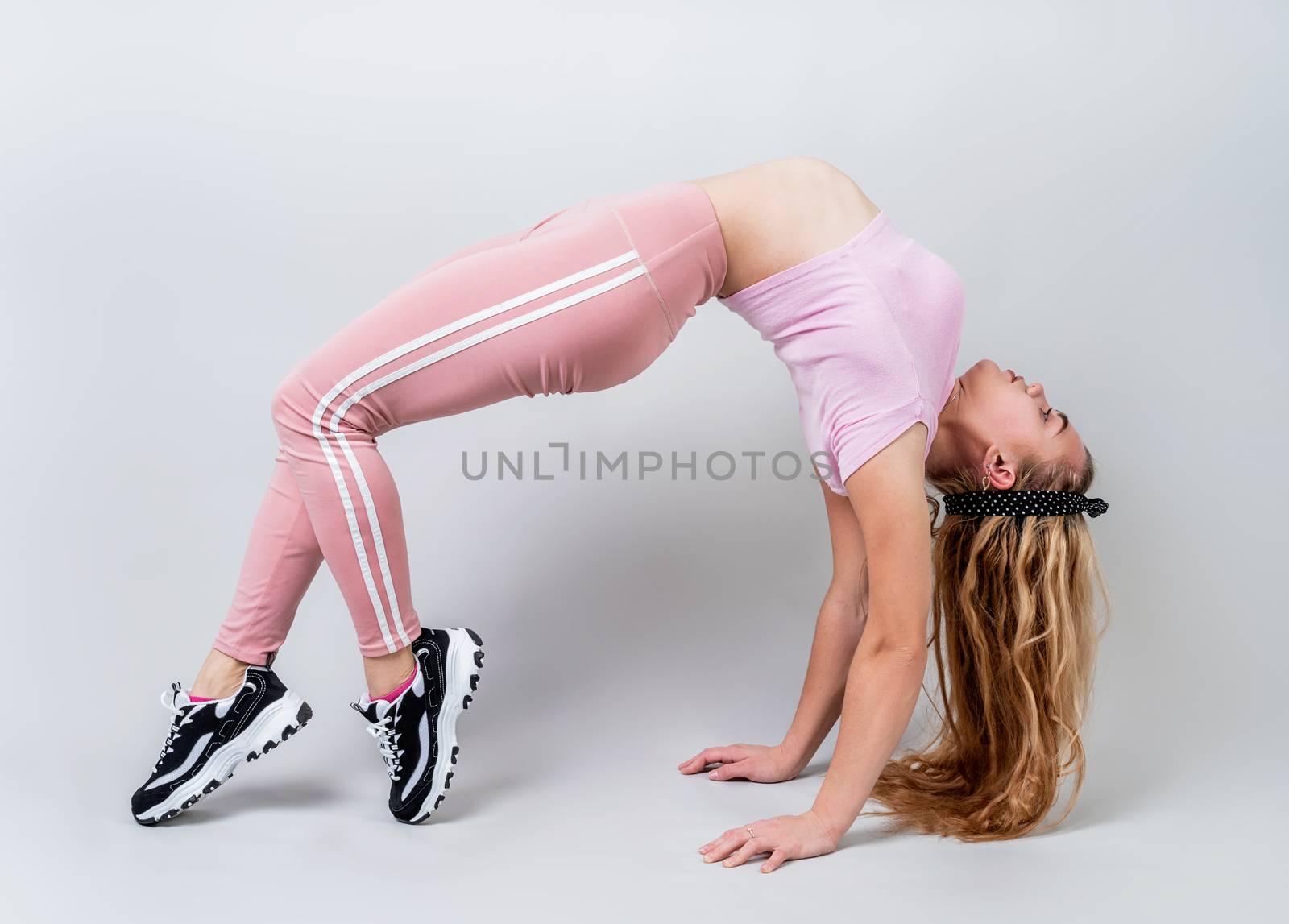 Fitness, sport, training and lifestyle concept. Acrobat woman wearing pink sportswear in a bridge pose in the studio isolated on gray background