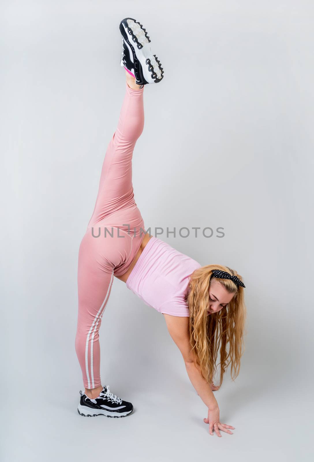 Acrobat woman wearing pink sportswear working out in the studio isolated on gray background by Desperada