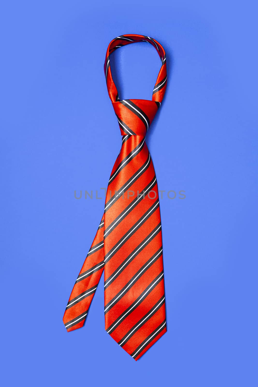 Red men's striped tie taken off for leisure time, isolated on blue background.