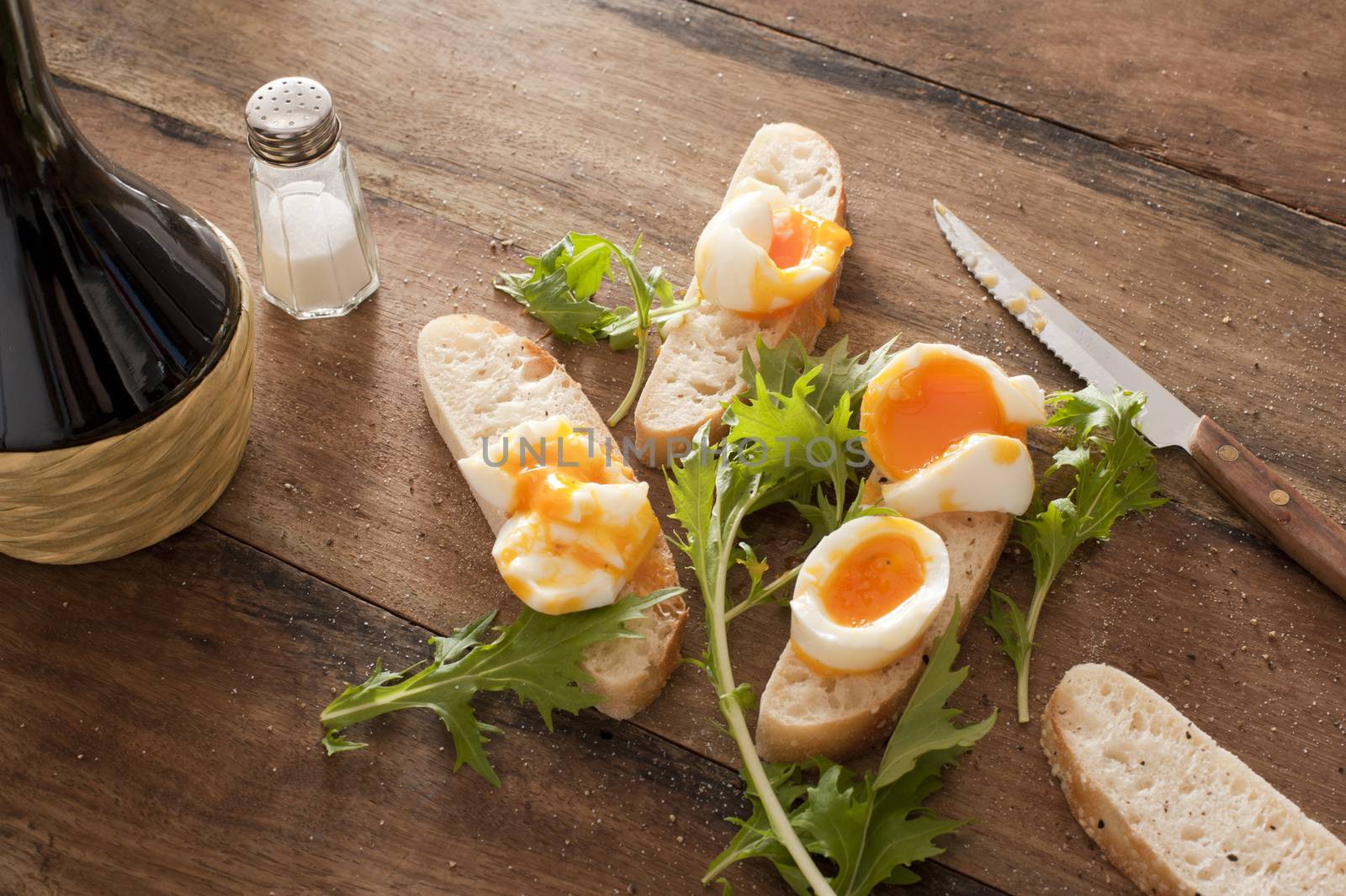 Fresh rolls with boiled eggs and rocket lying on a wooden table with salt and a knife for preparing delicious open sandwiches for breakfast