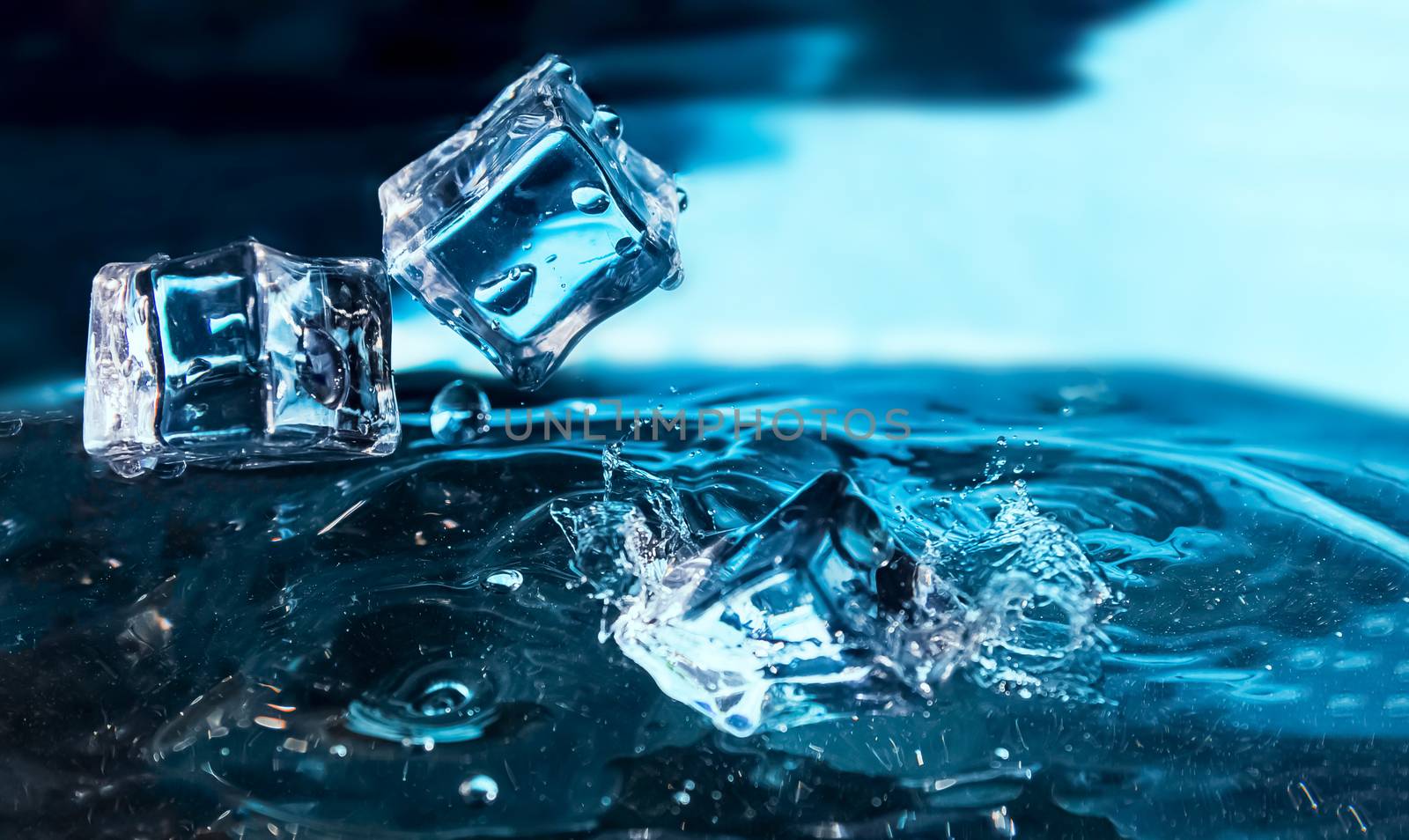 Ice cubes falling into the blue water. Splash of ice water. Water splashes from falling ice cubes.