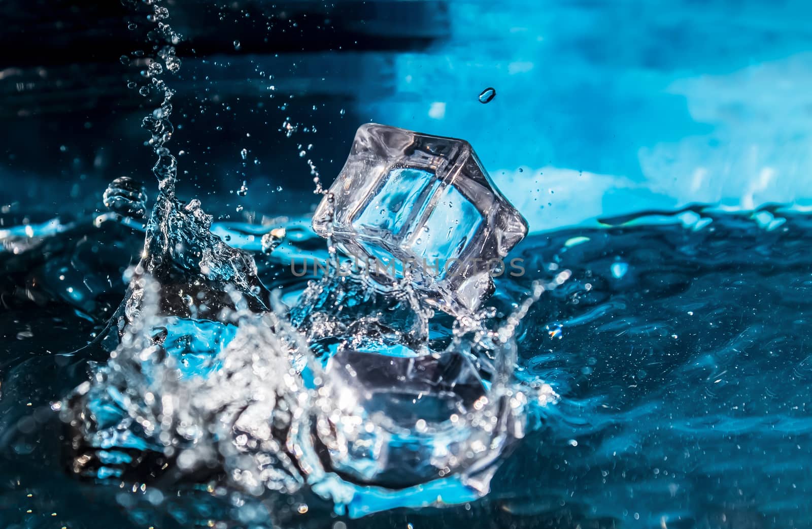 Ice cubes falling into the blue water. Splash of ice water. Water splashes from falling ice cubes.