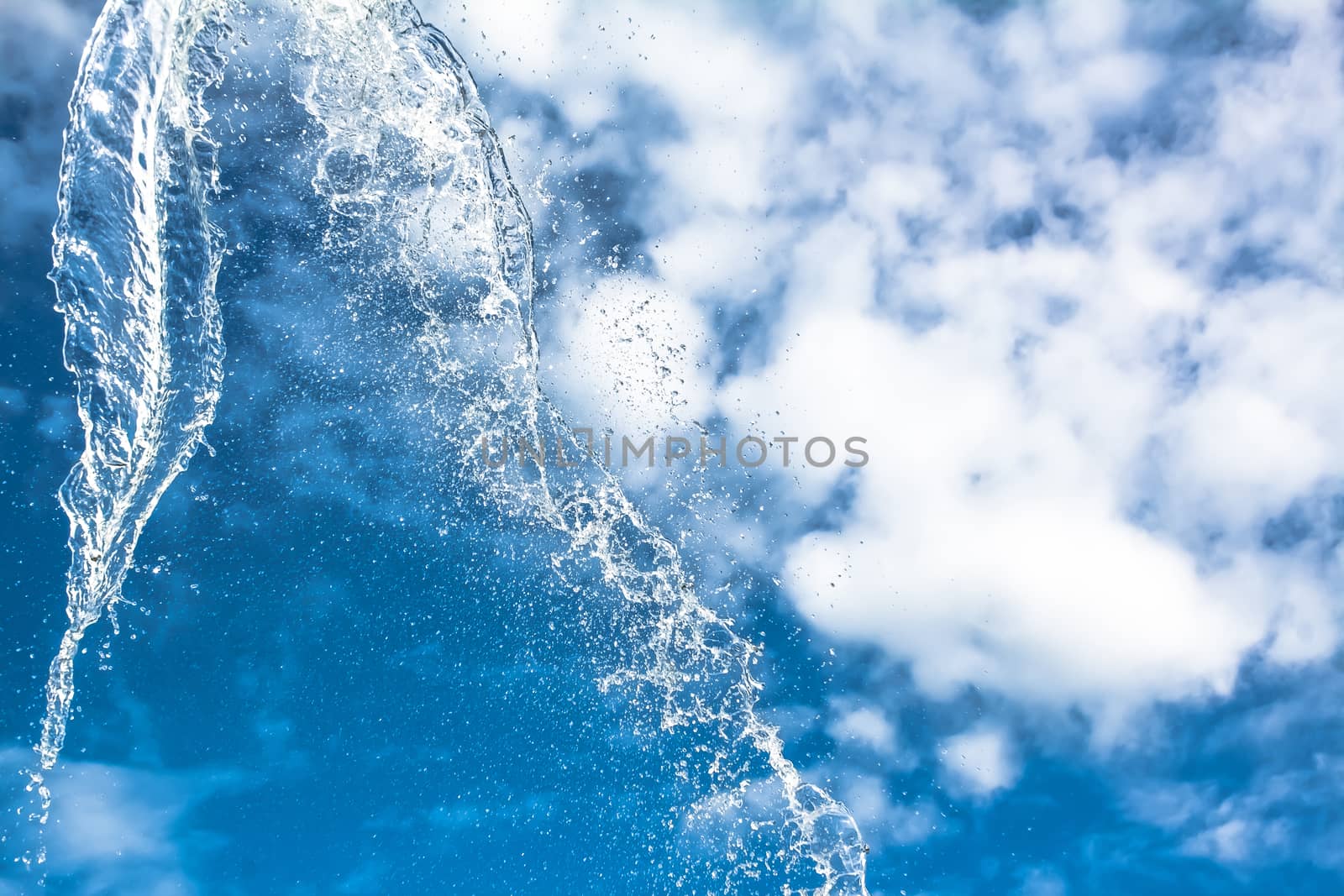 Splashes of water against a blue sky with clouds. A splash of water against the sky.