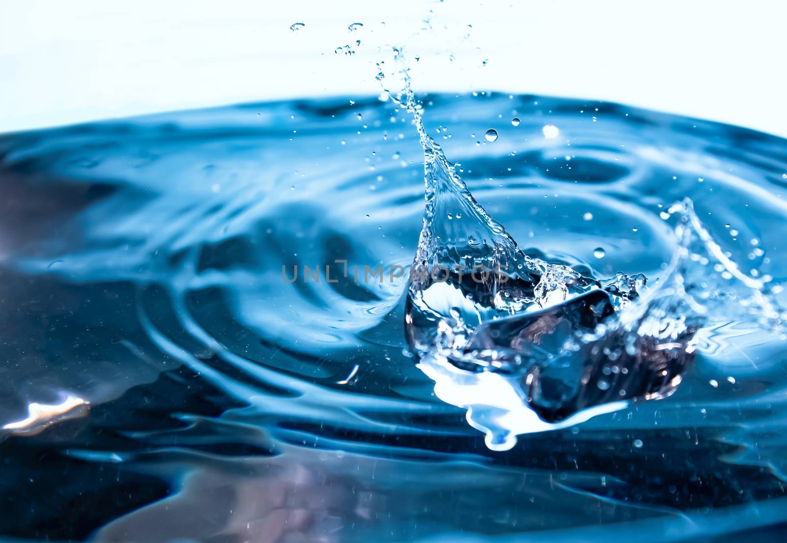 Water splash. Ice cubes falling into the blue water. Splash of ice water. Water splashes from falling ice cubes