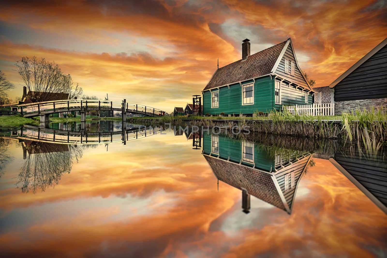 Reflection of the wooden green houses topped with dark orange color roof reflected on the calm water of the canal