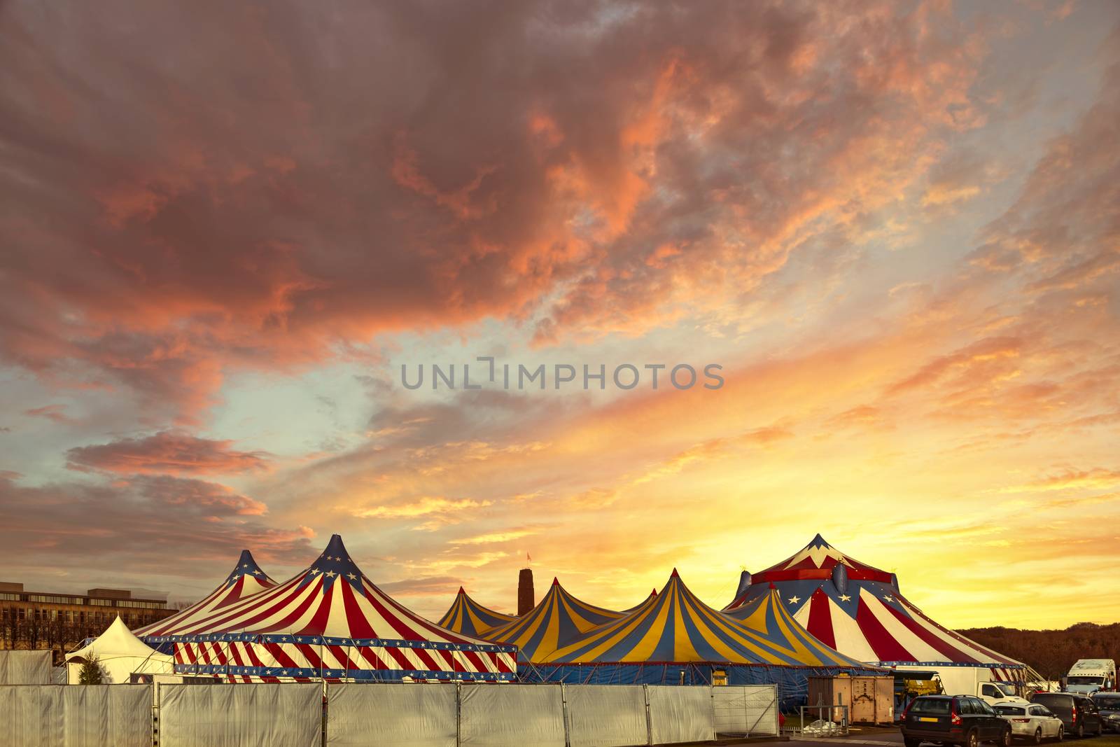 Red and white circus tents topped with bleu starred cover against a sunny blue sky with clouds by ankorlight