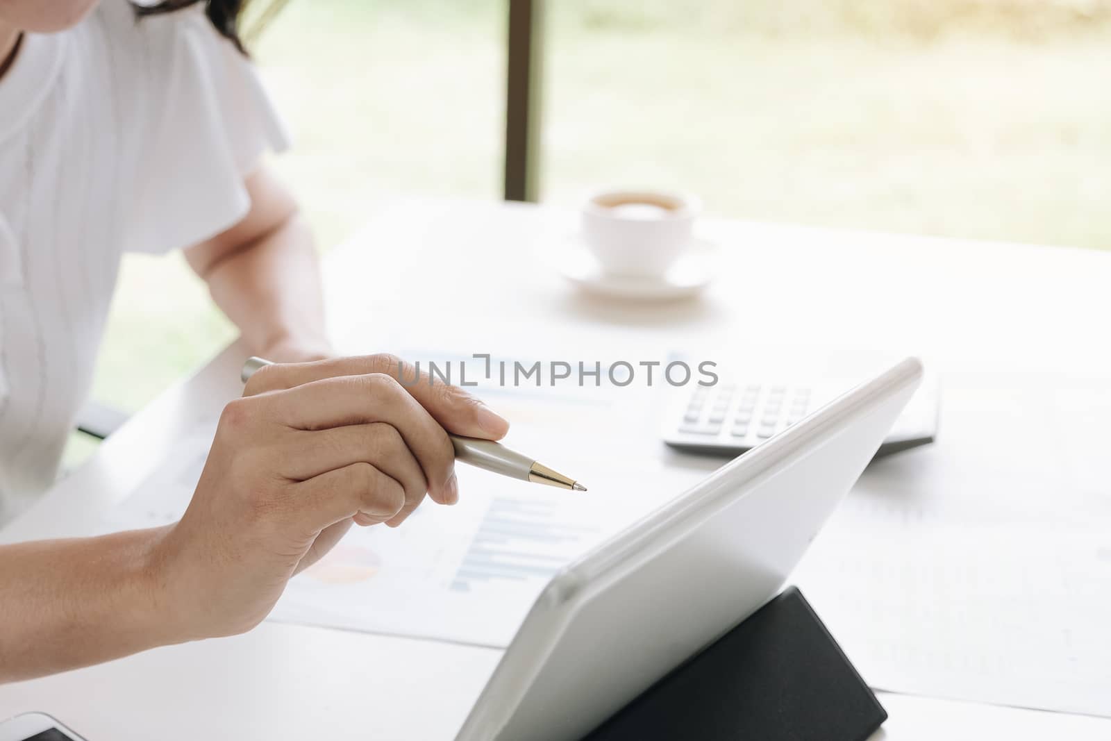 Business woman hand holding pen pointing at screen of laptop com by wichayada