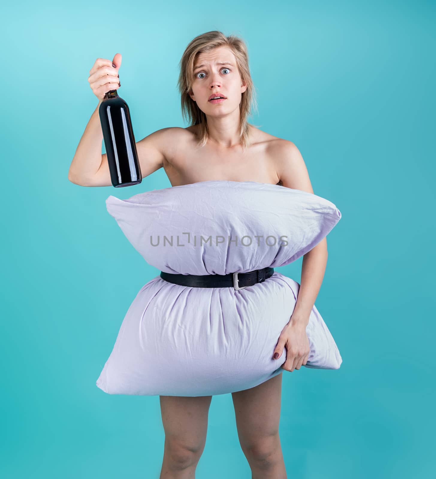 Desperate woman in pillowdress holding a wine bottle isolated on blue background by Desperada