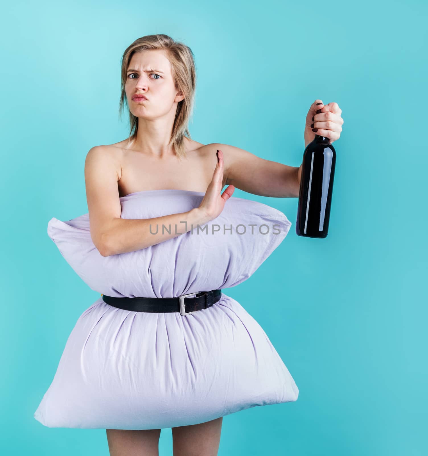 Coronavirus quarantine. Crazy quarantine. Blonde woman in pillowdress holding a wine bottle showing denying gesture isolated on blue background. Pillow challenge