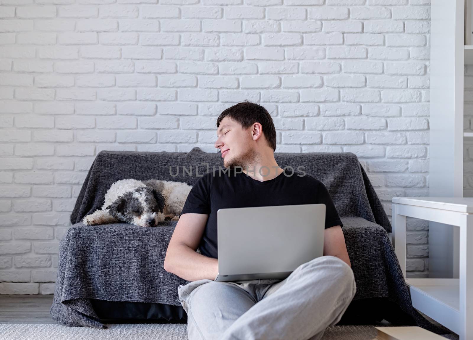 Young funny man enjoying time with his bichon frise dog working on the laptop by Desperada