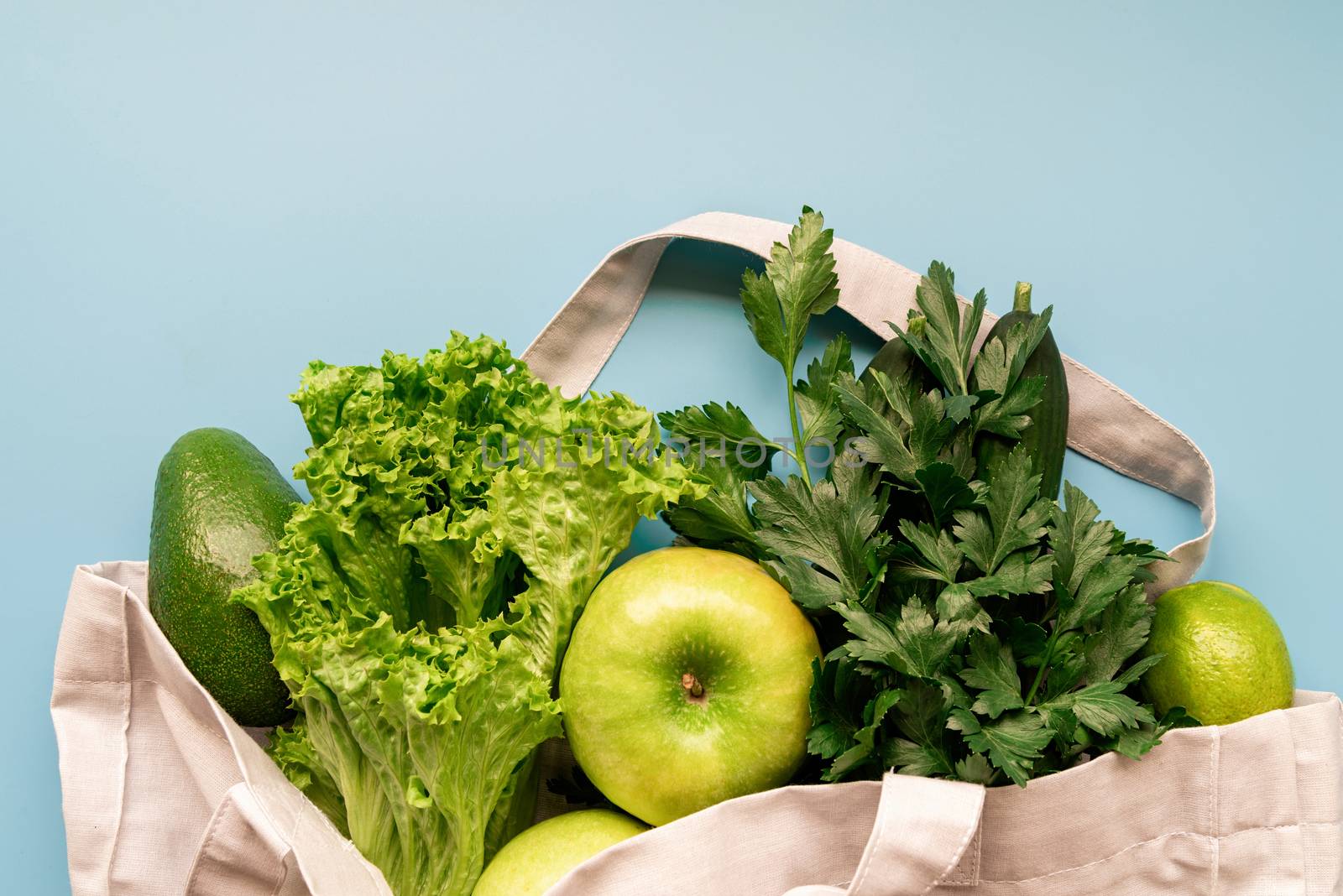 Coronavirus food supplies concept. Food layout with apples, lettuce, cucumbers, limes, parsley in eco friendly bag on blue background. Flat lay. Copy space.