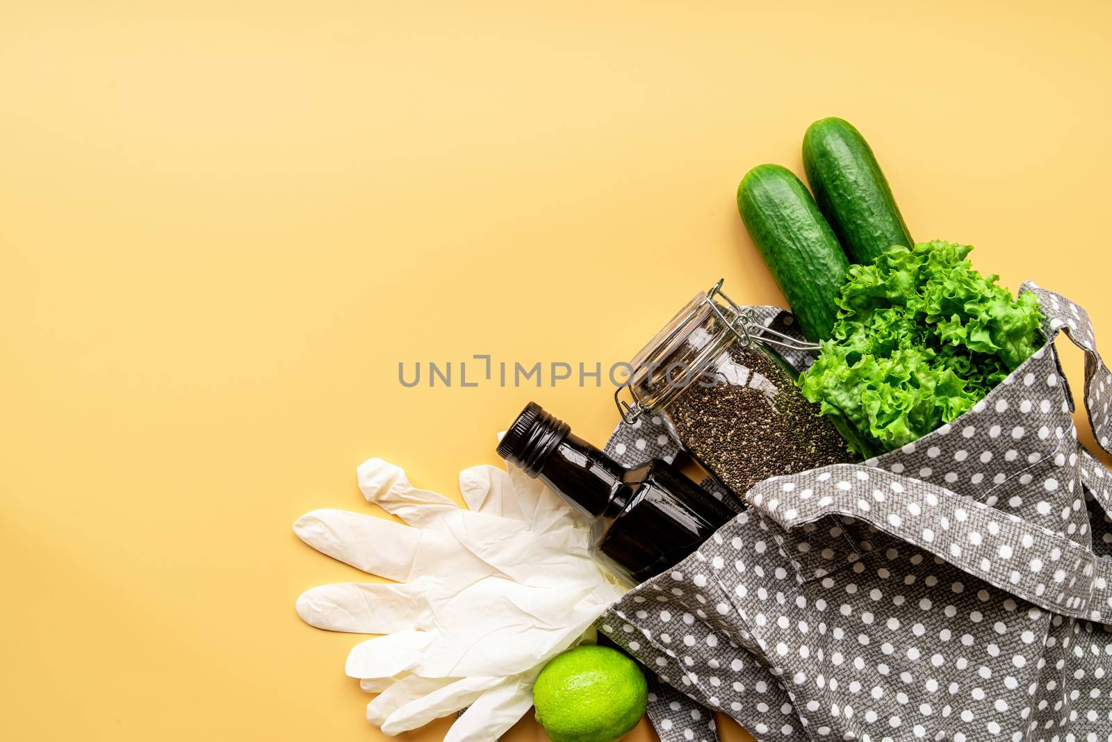 Coronavirus food supplies concept. Food layout with green vegetables, lettuce, olive oil, chia seeds, gloves in eco friendly bag on orange background. Flat lay. Copy space.