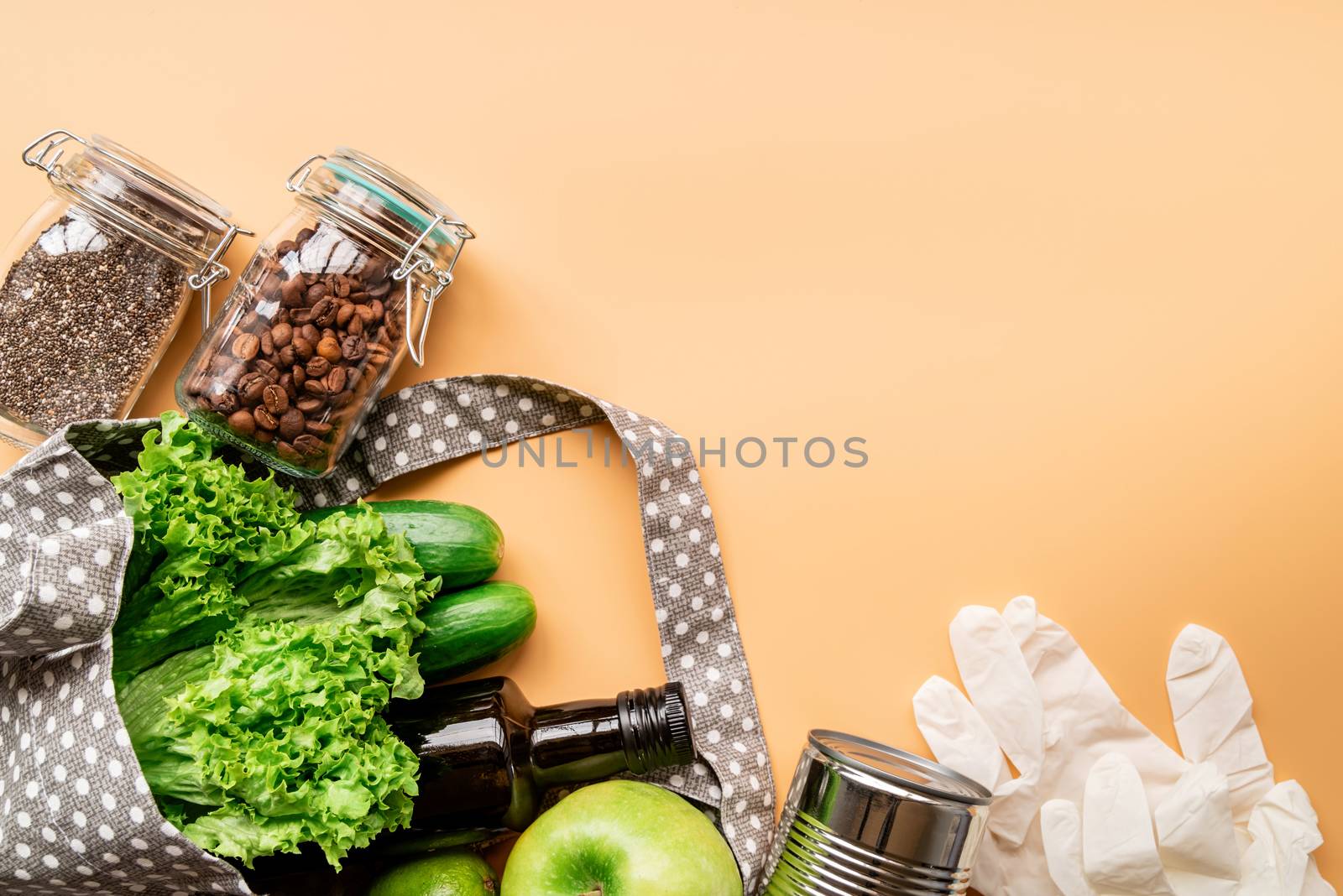 Coronavirus food supplies concept. Food layout with green vegetables, lettuce, olive oil, chia seeds, gloves in eco friendly bag on orange background. Flat lay. Copy space.
