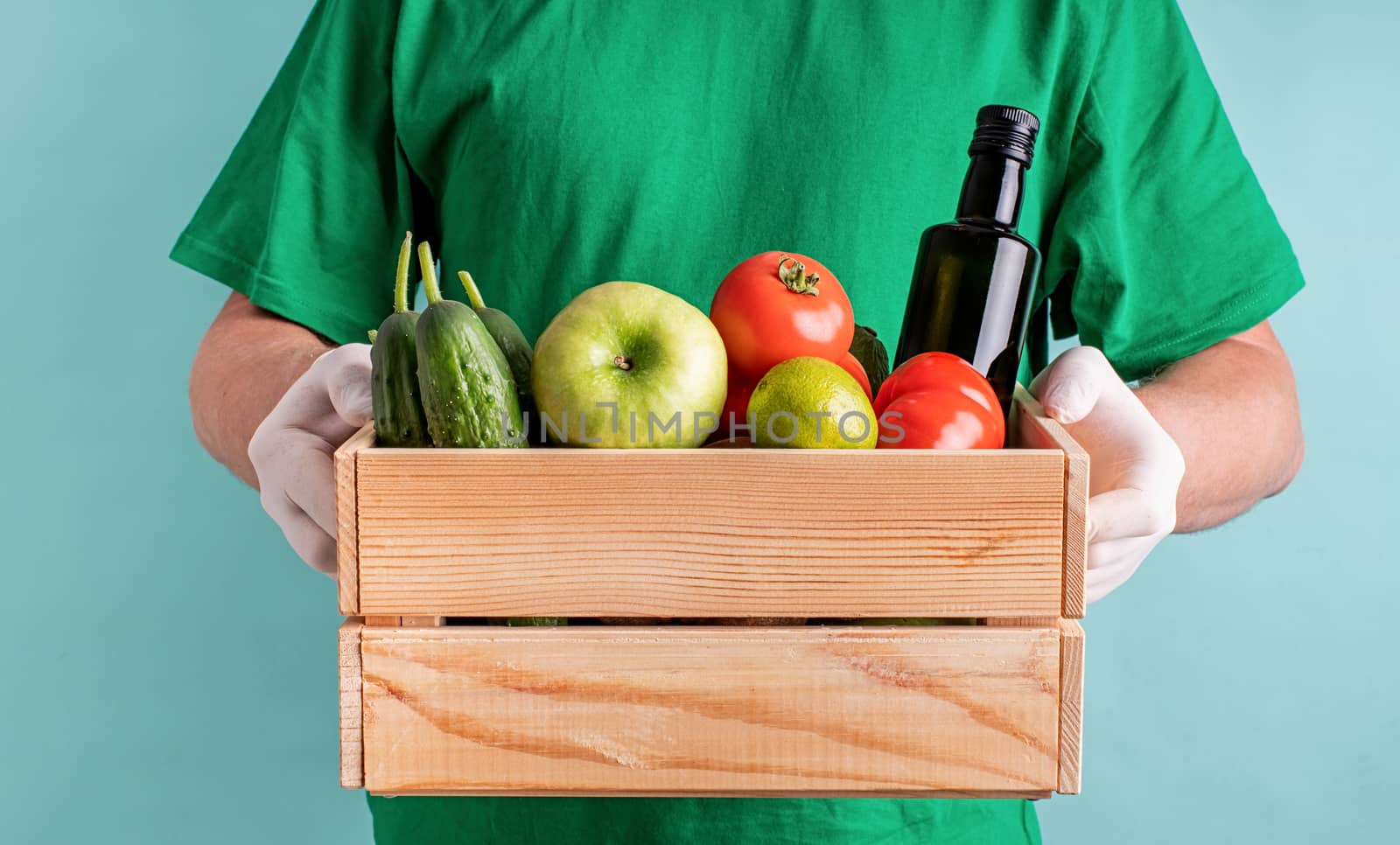 Man in gloves holding a wooden box full of vegetables by Desperada