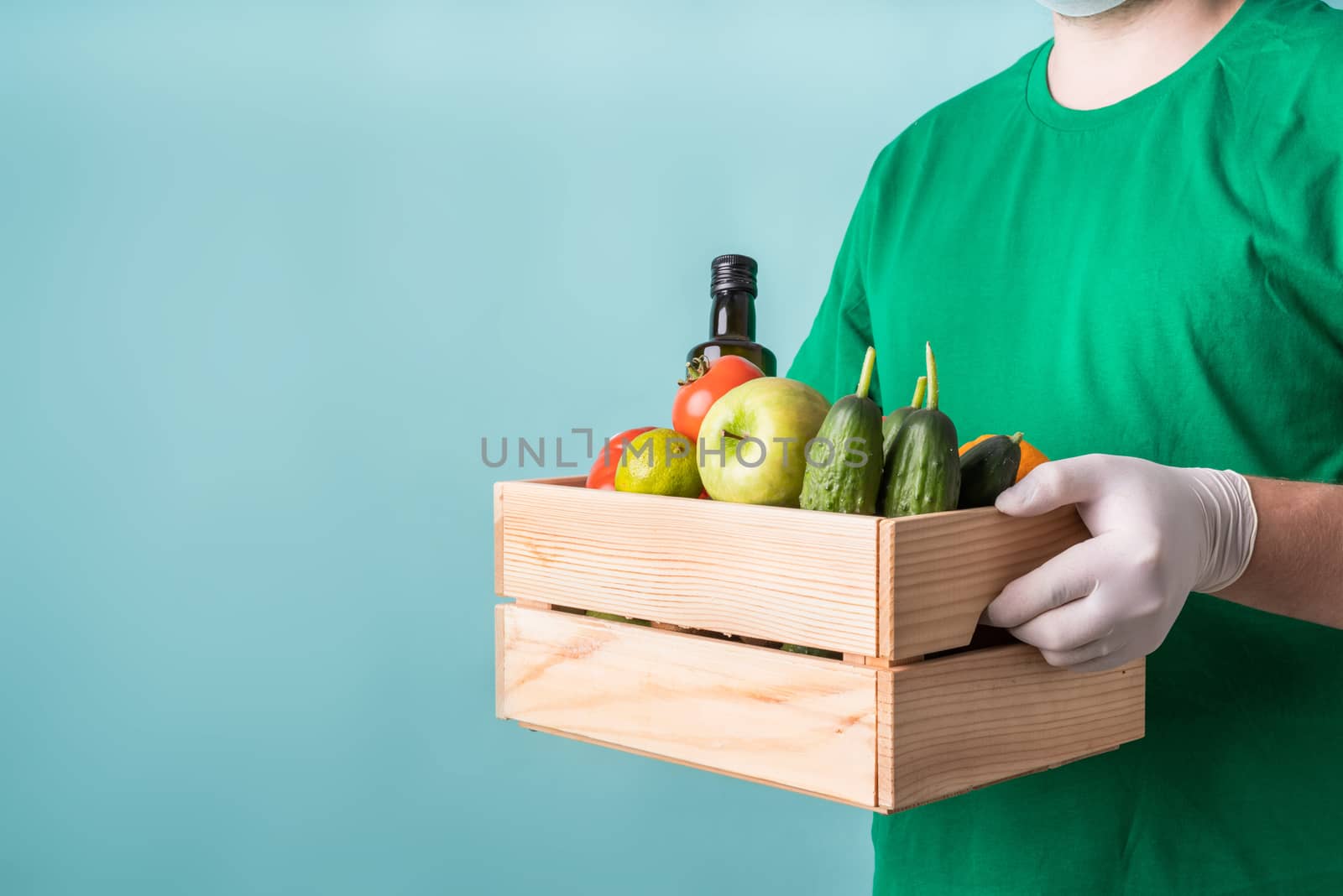 Man in gloves holding a wooden box full of vegetables by Desperada