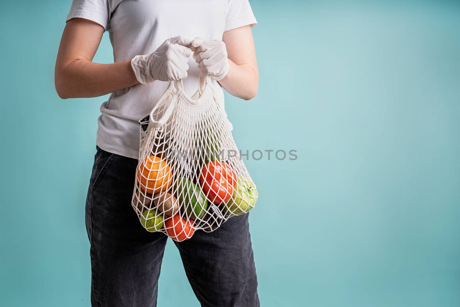 woman in gloves holding mesh bad with vegetables isolated on blue background with copy space by Desperada