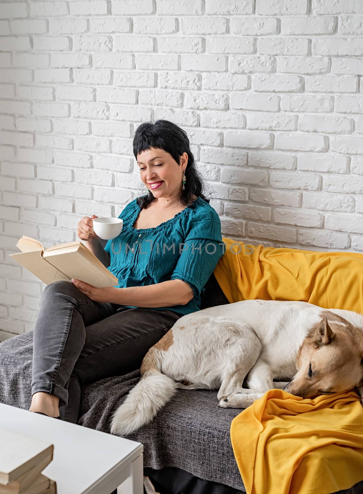 Stay home. Pet care. Smiling middle aged woman enjoying being at home and reading sitting on the sofe
