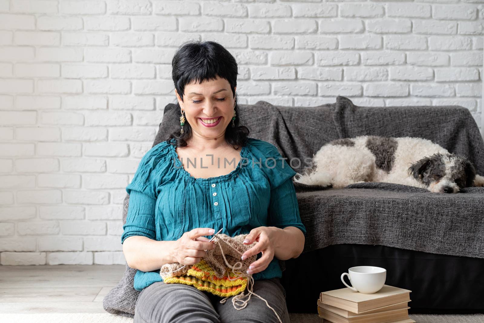 Stay home. Copy space. Smiling middle aged woman enjoying being at home and knitting sitting on the sofa