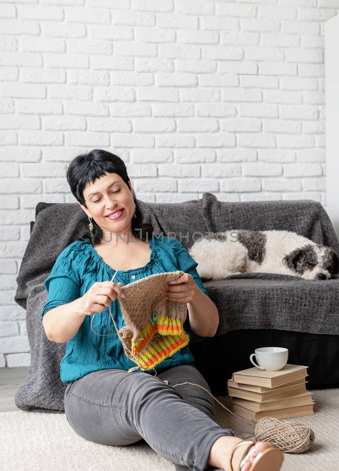 Charming middle aged woman enjoying being at home and knitting sitting on the sofa by Desperada