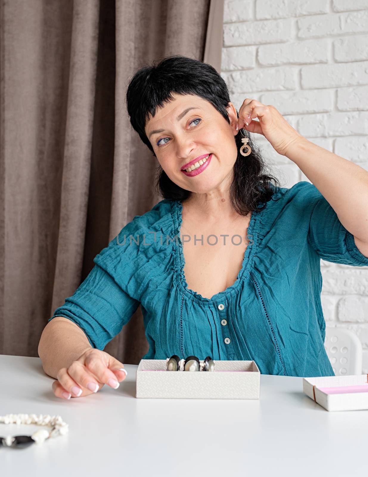 Beautiful smiling middle aged woman trying on the jewelery sitting at the table