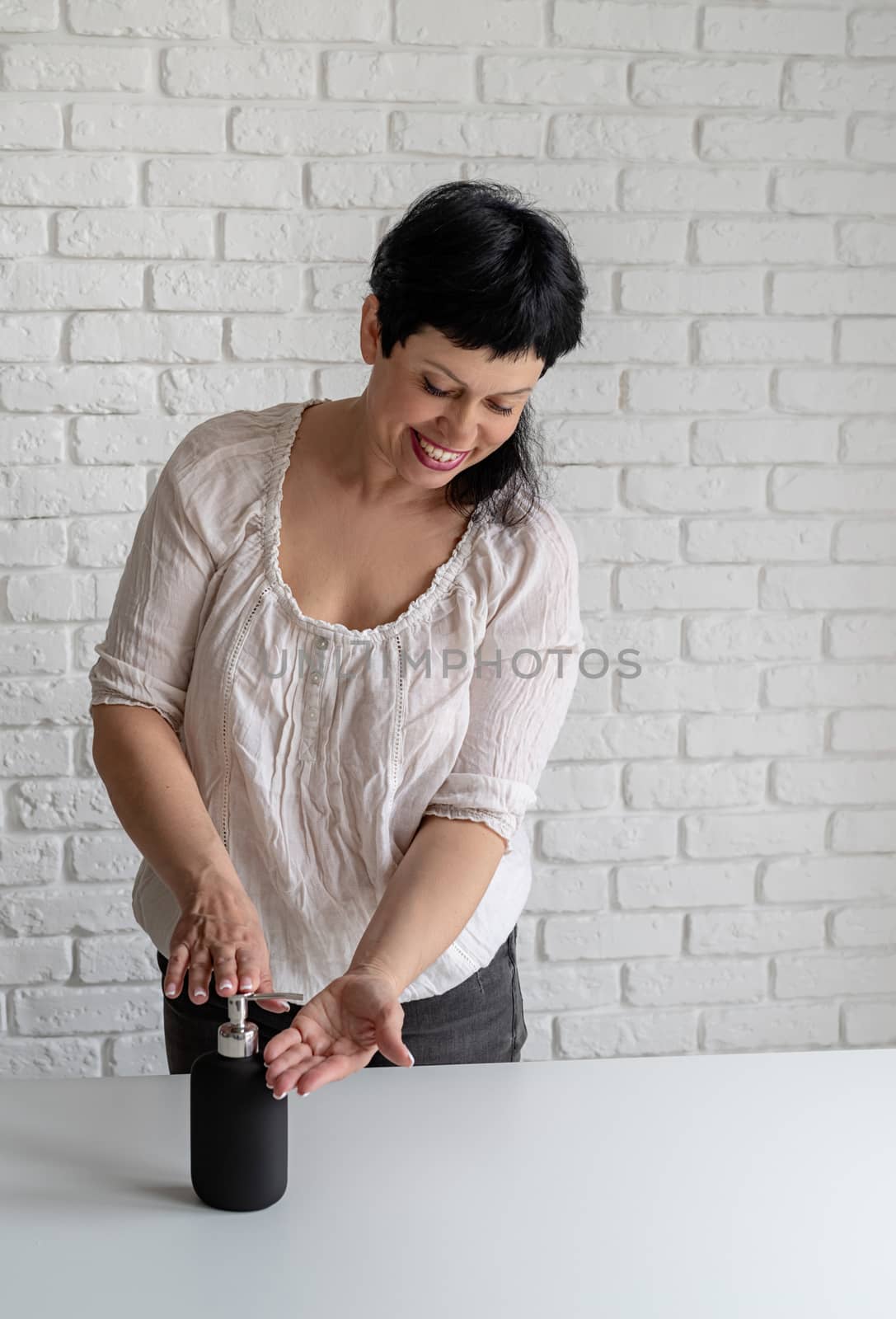 Middle aged woman hands using sanitizer gel pump dispenser with copy space