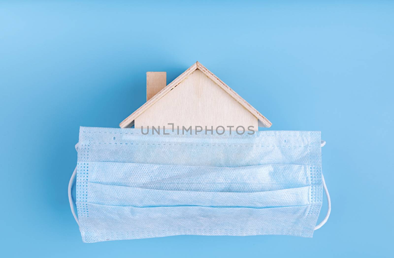 Stay home. Self quarantine. Wooden house covered with the mask top view flat lay