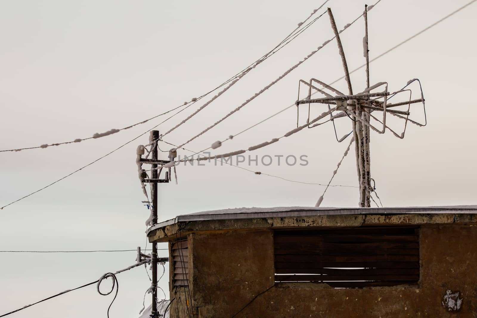 old frozen roof antenna at winter night with selective focus on small city background.