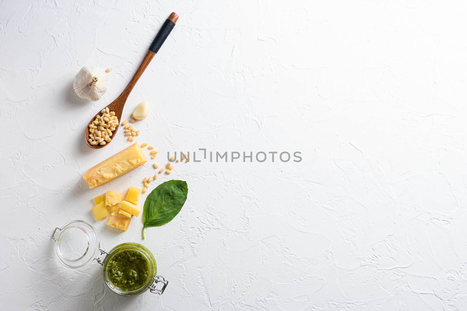 classic Basil pesto sauce in a glass jar. fresh basil leaves, grated parmesan cheese, pine nuts, garlic, with wood spoon white table concrete from above top view by Ilianesolenyi