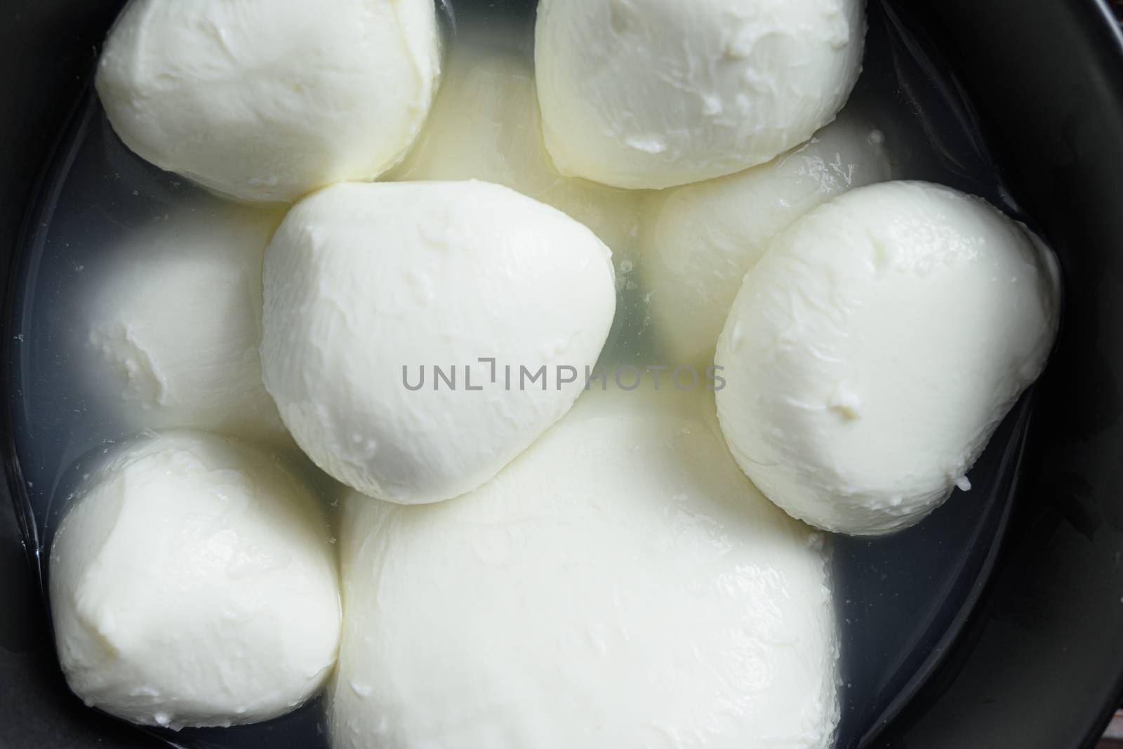 Mozzarella cheese buffalo balls in black bowl close up top view overhead.