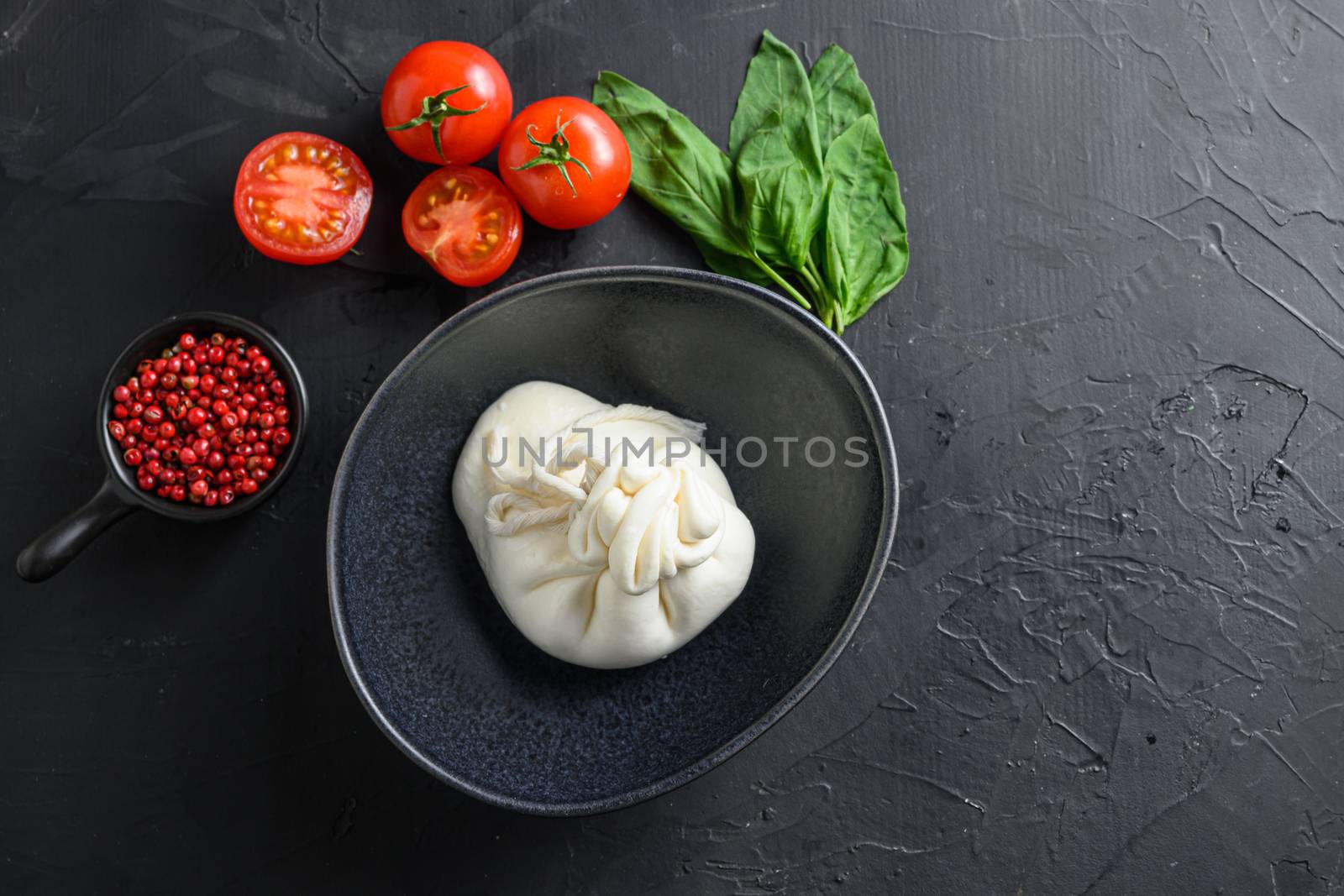 burrata Italian cheese in black bowl with tomatoes basil on black surface space for text.