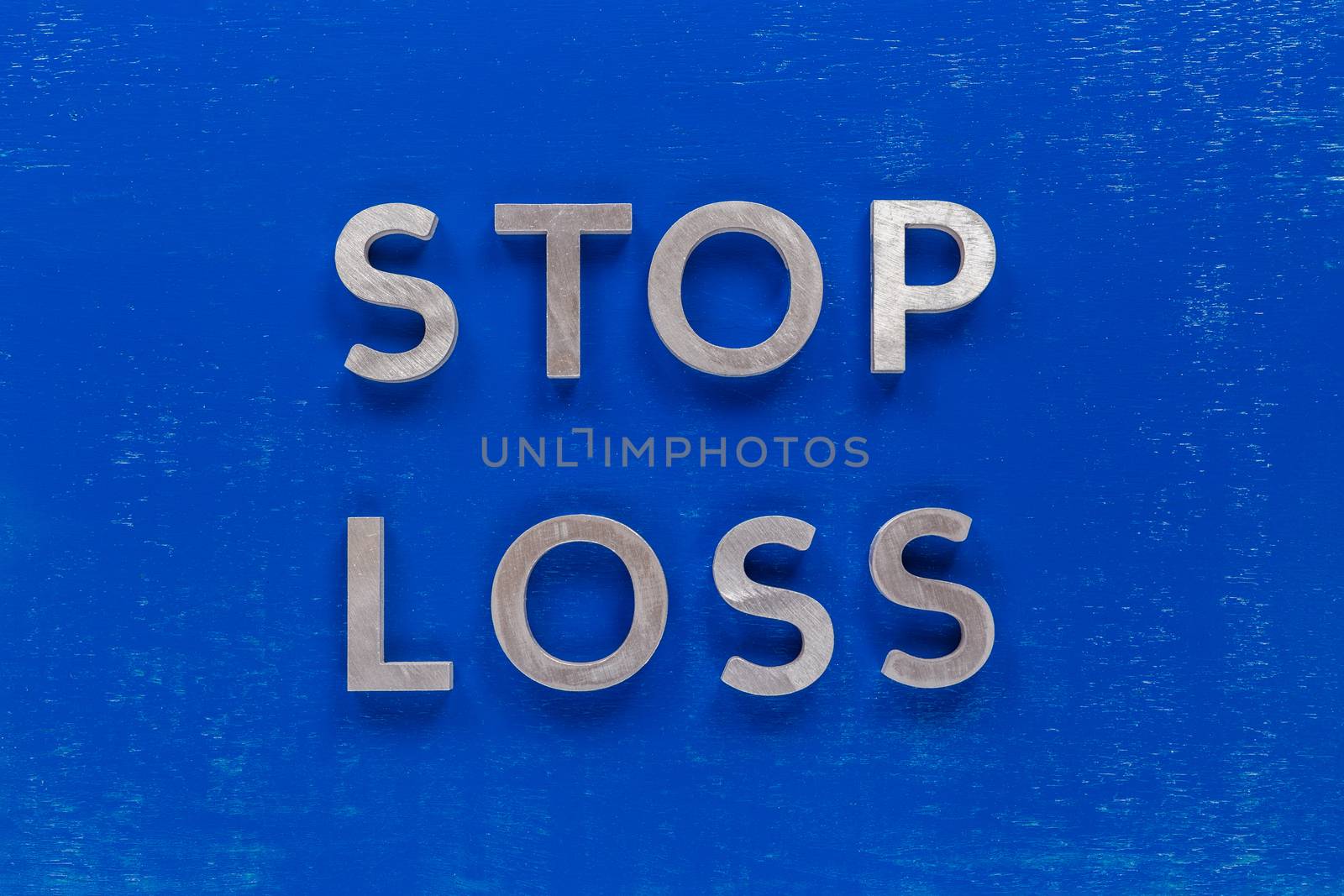 The phrase stop loss laid on blue painted board with thick silver metal aphabet characters. by z1b