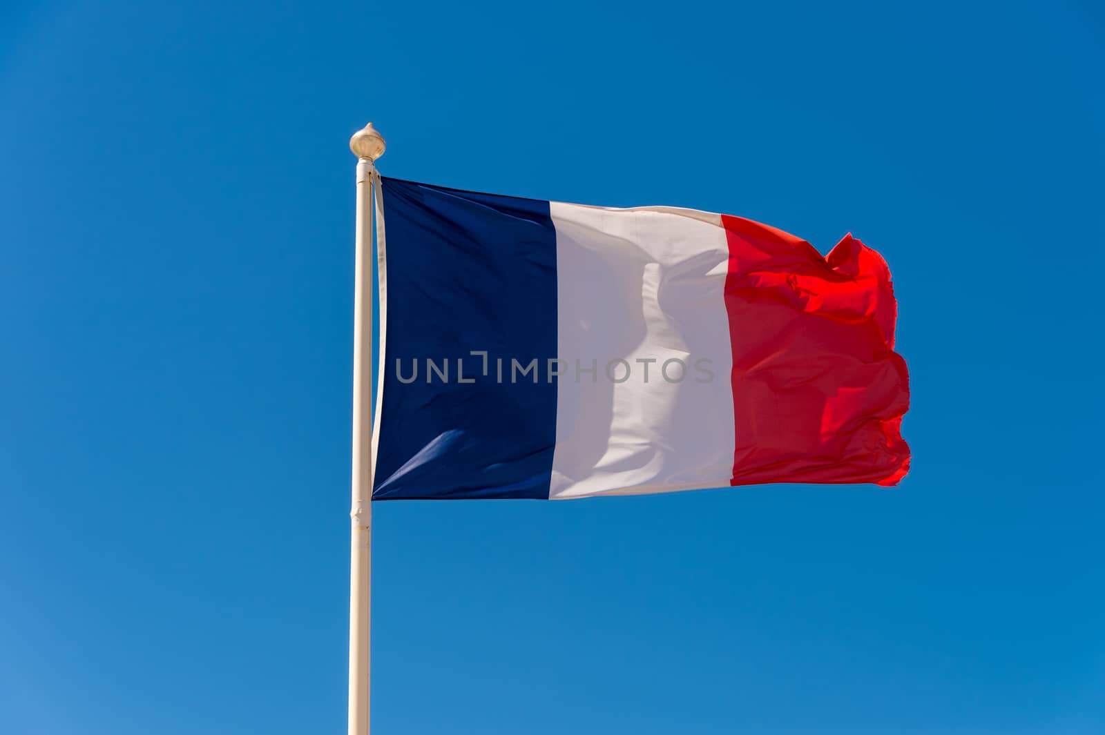 French flag waving against blue sky in Wimereux, France.