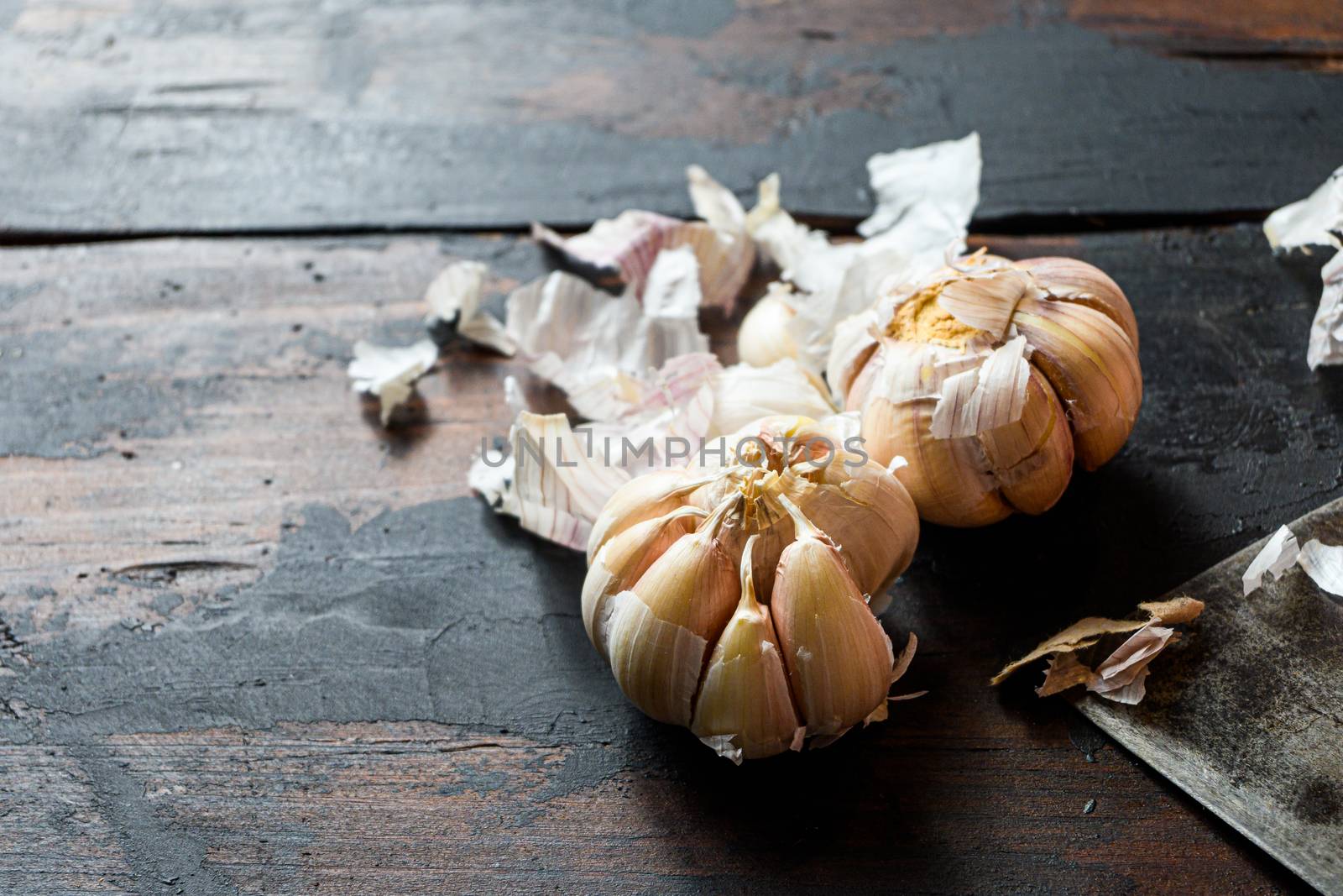 Garlic, which lies near the cutting knife with raw meat beef steak. Raw beef meat prepared for cooking steaks. Beside the ingredients for cooking steaks, spices and herbs rosemary garlic. Side view Close up macro.