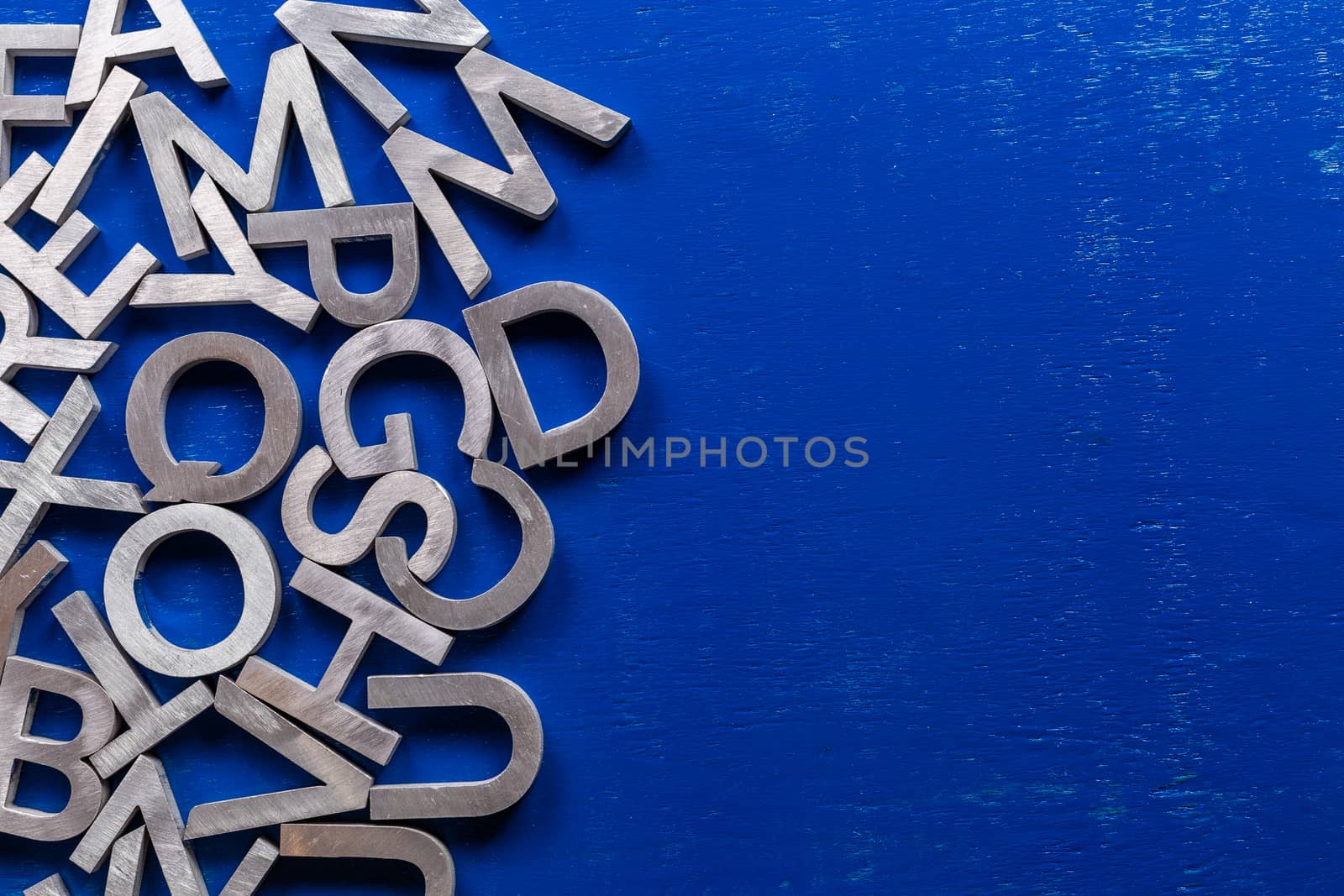 Flat mockup of silver metal alphabet characters on blue painted board background with copyspace. by z1b