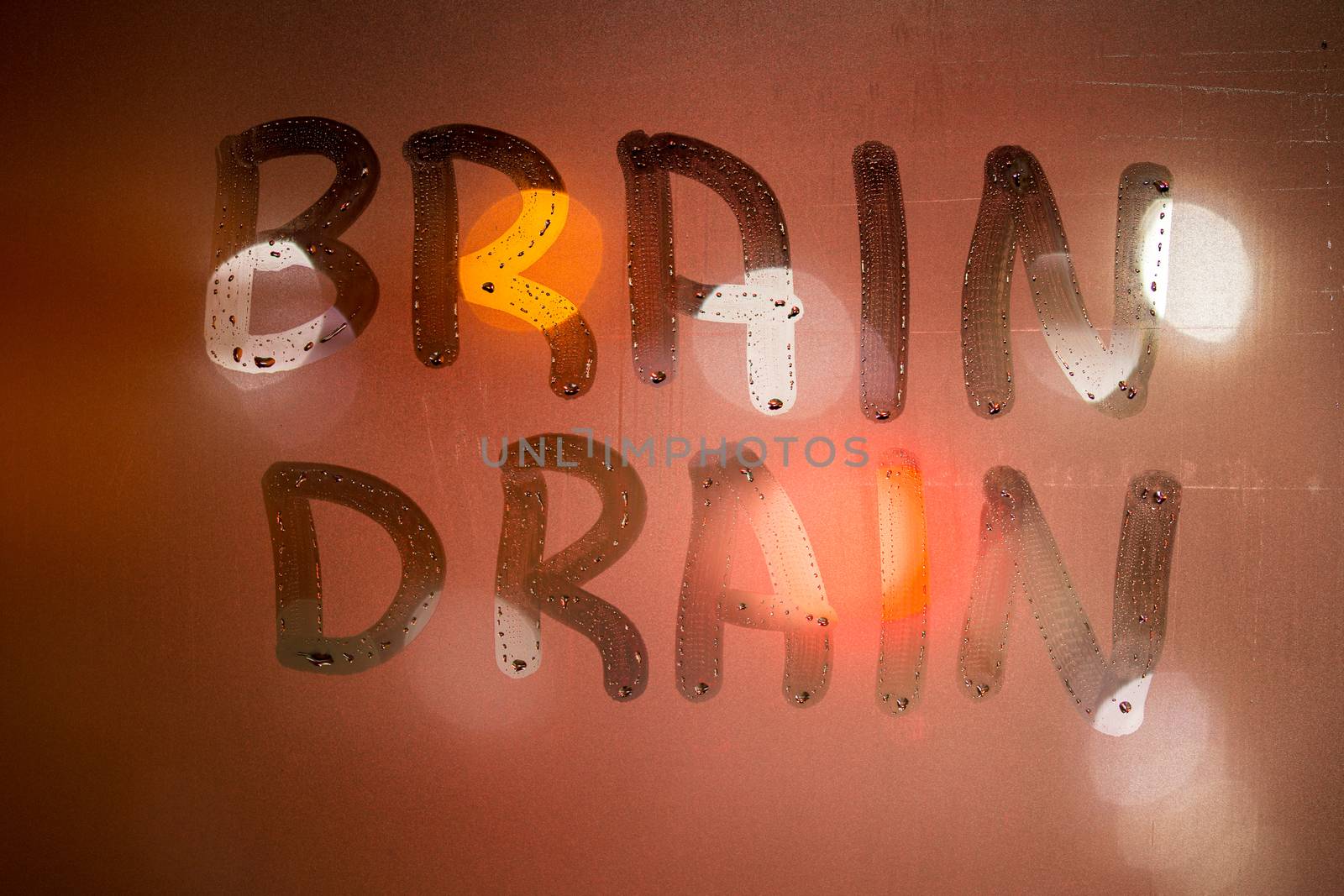 the word brain drain written on night wet window glass close-up with blurred background in in orange colors.