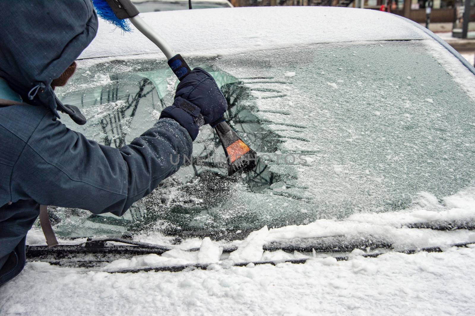 Man cleaning car windshield from ice with scraper tool. by mbruxelle