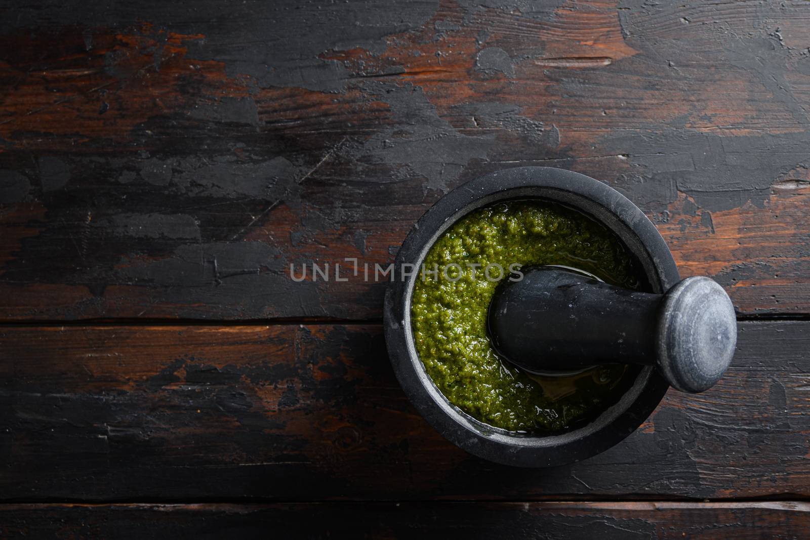 fresh Green basil pesto preparation in black mortar over old wood table copy space for text overhead.