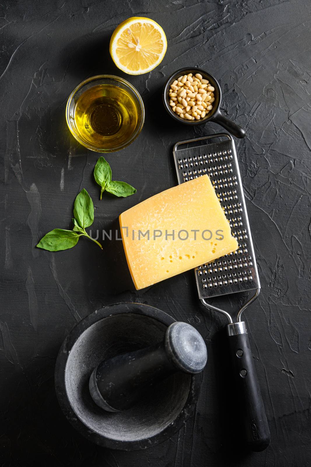 ingredients for green pesto over black stone background Parmesan cheese, basil leaves, pine nuts, olive oil, garlic mortar top view.