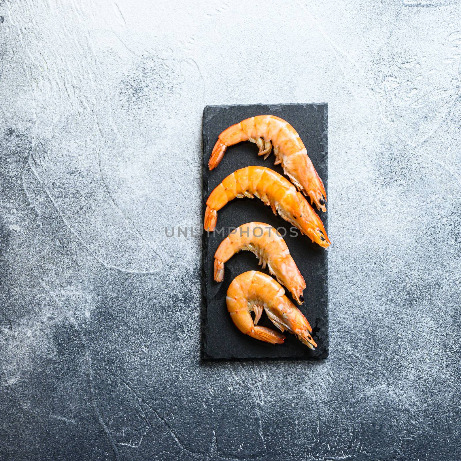 shrimp on a stone cutting board over textured grey white backgrounnd, top view, closeup space for text.