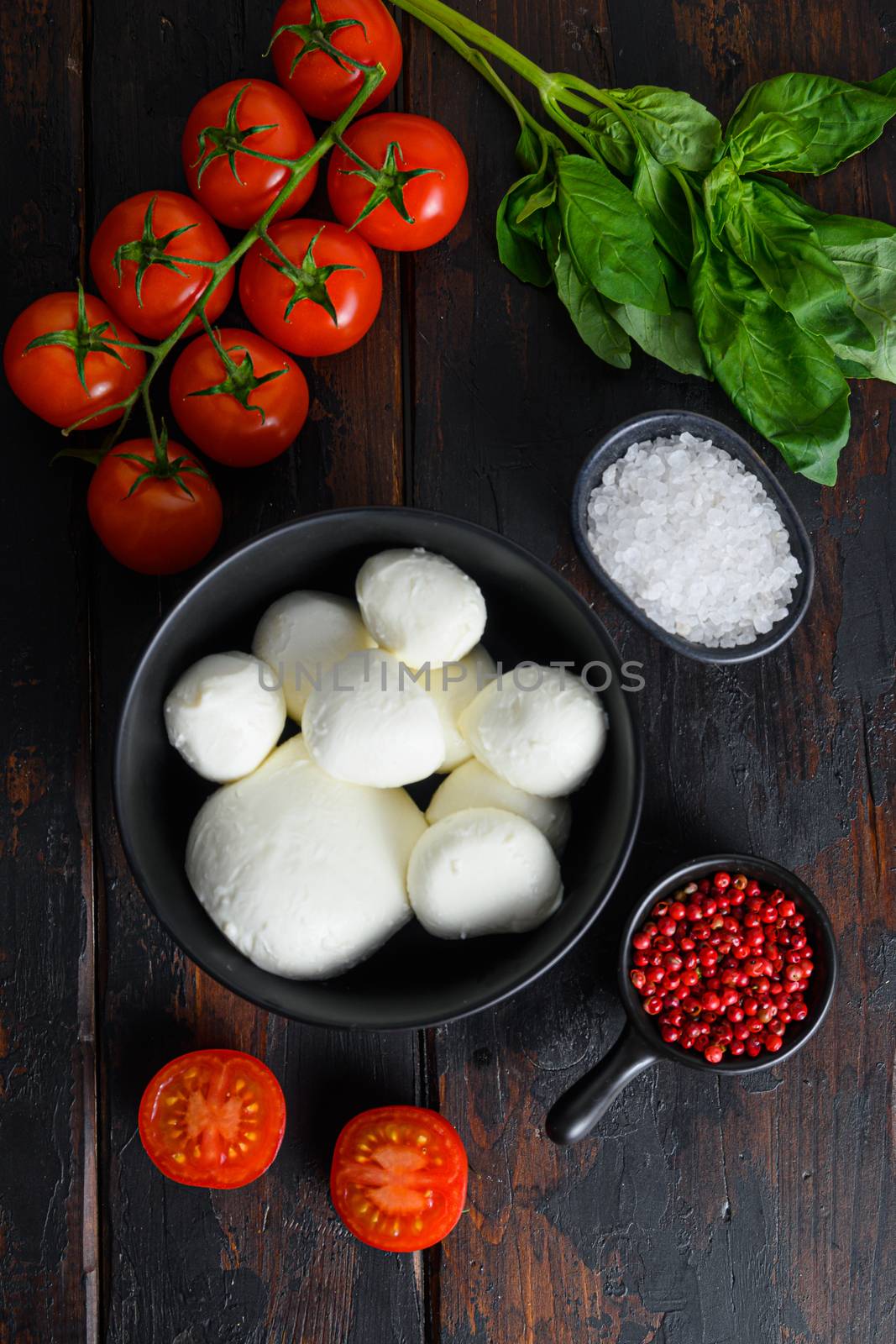 Mozzarella cheese balls, cherry tomatoes and green fresh organic basil peppercorns on wood table by Ilianesolenyi