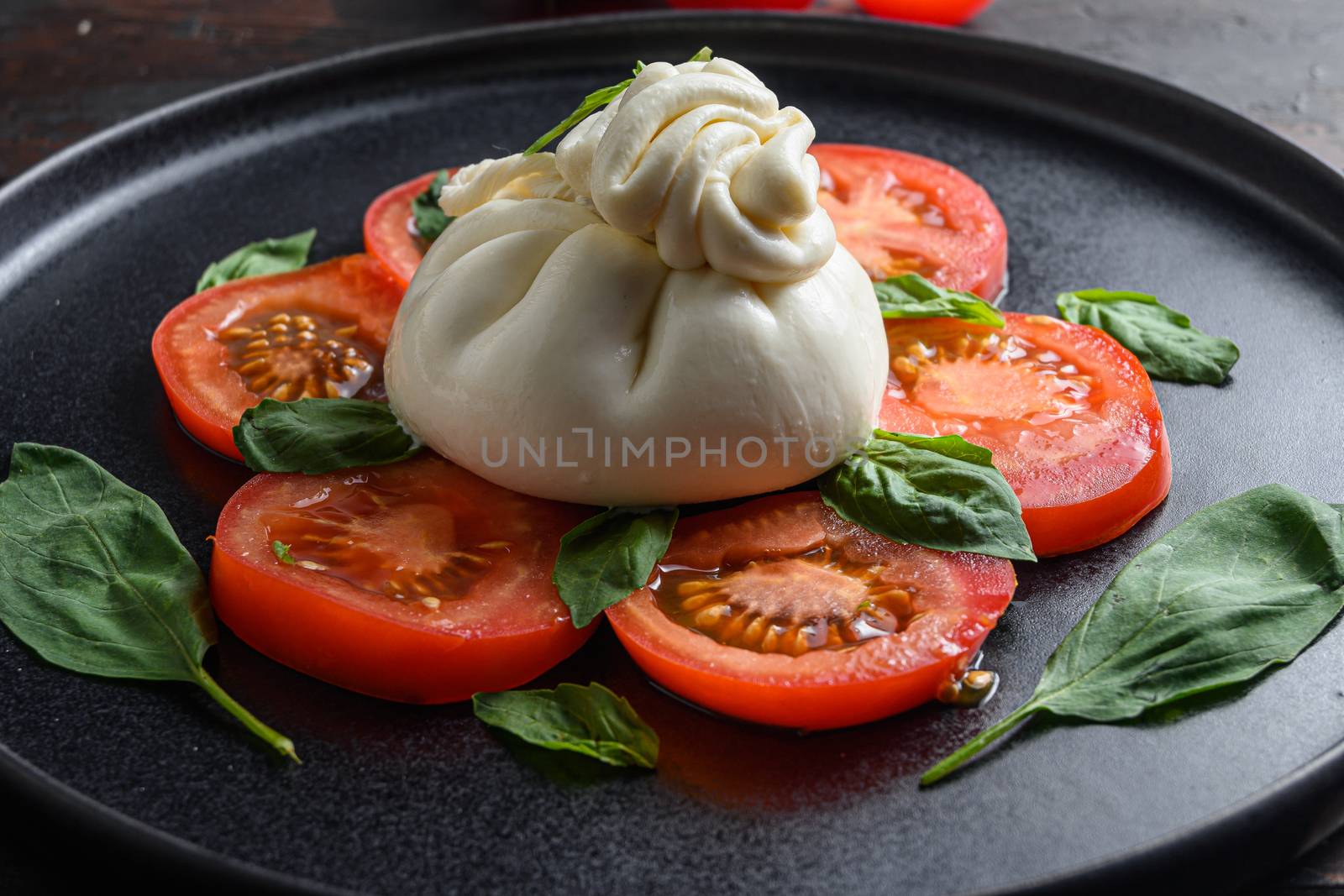 Handmade burrata cheese served with fresh tomatoes and basil leaves traditional italian Salad close up by Ilianesolenyi