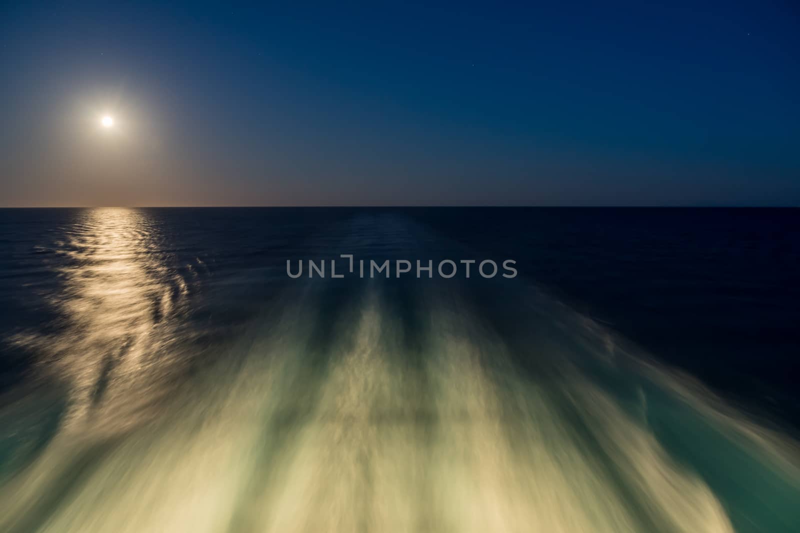 Moon rising over wake and waves of cruise ship at sea with concept of leaving or starting anew