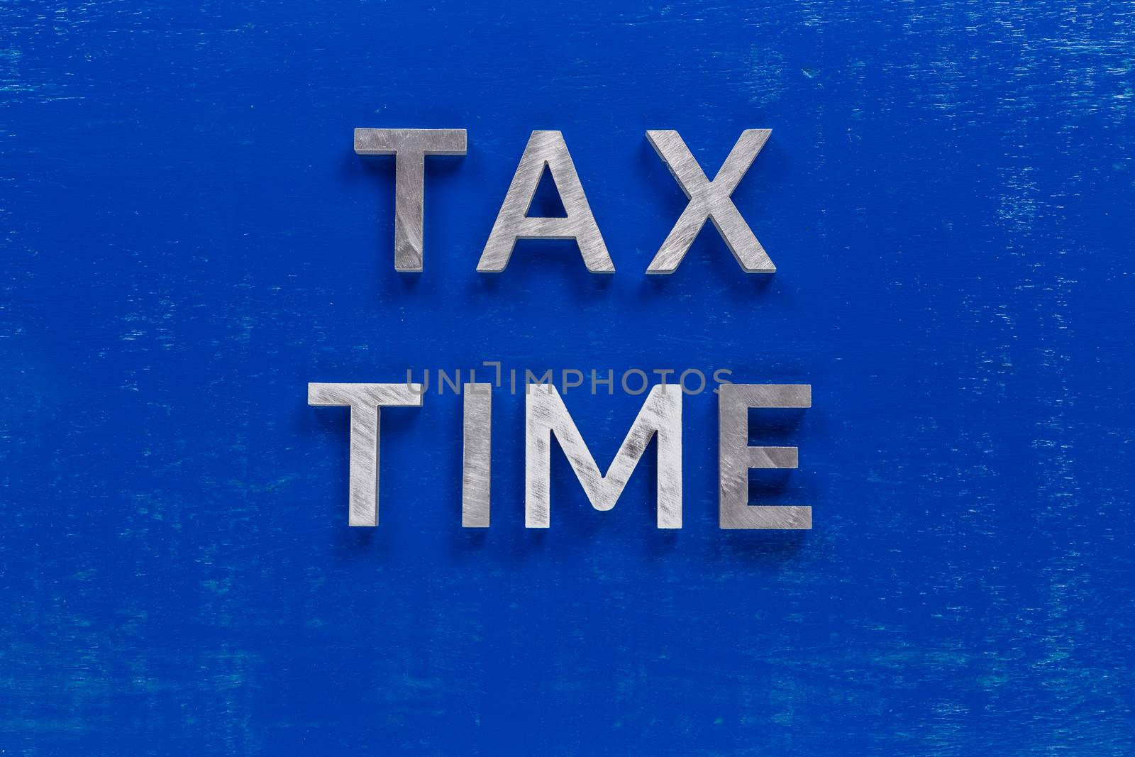 the words tax time layed on blue painted board with thick silver metal aphabet characters.