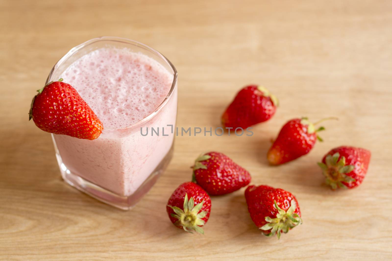 Fresh strawberry smoothie cold drink. Milkshake in glass on wooden table. Fruits for decoration