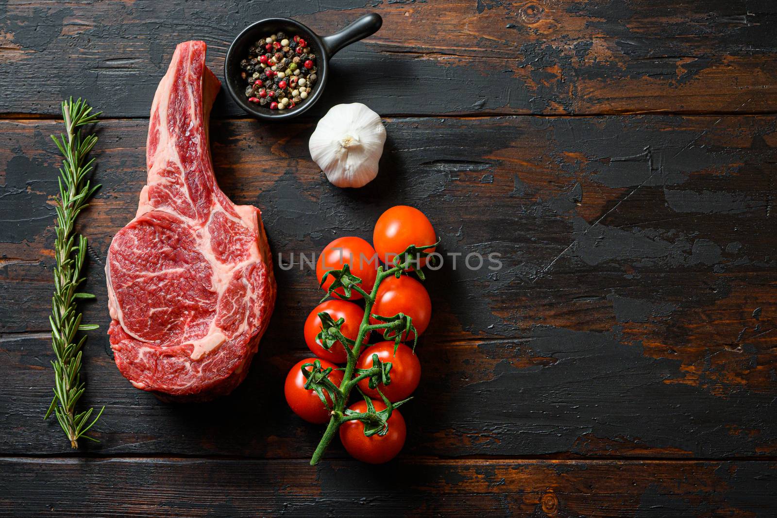 Raw uncooked black angus Dallas steak in rustic style on wooden table background. with tomato garlic herbs and peppercorns rosemary space for text top view by Ilianesolenyi